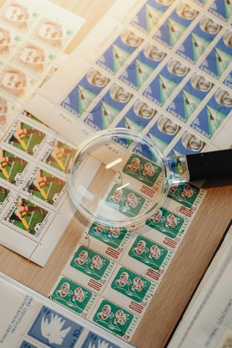 A close-up image of various vintage postage stamps being examined with a magnifying glass on a wooden surface.
