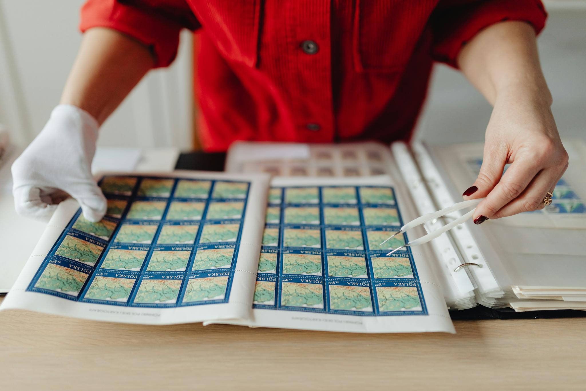 A person wearing gloves carefully handling a collection of vintage postage stamps using tweezers.