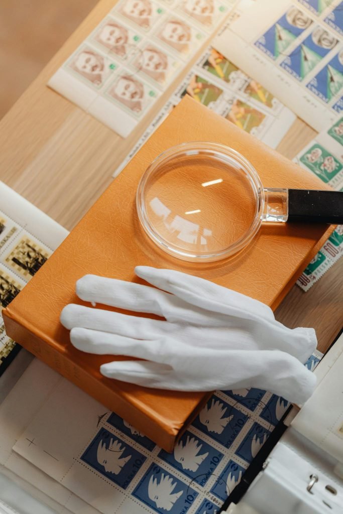 High angle view of a vintage stamp collection featuring a magnifying glass and gloves on a wooden surface.