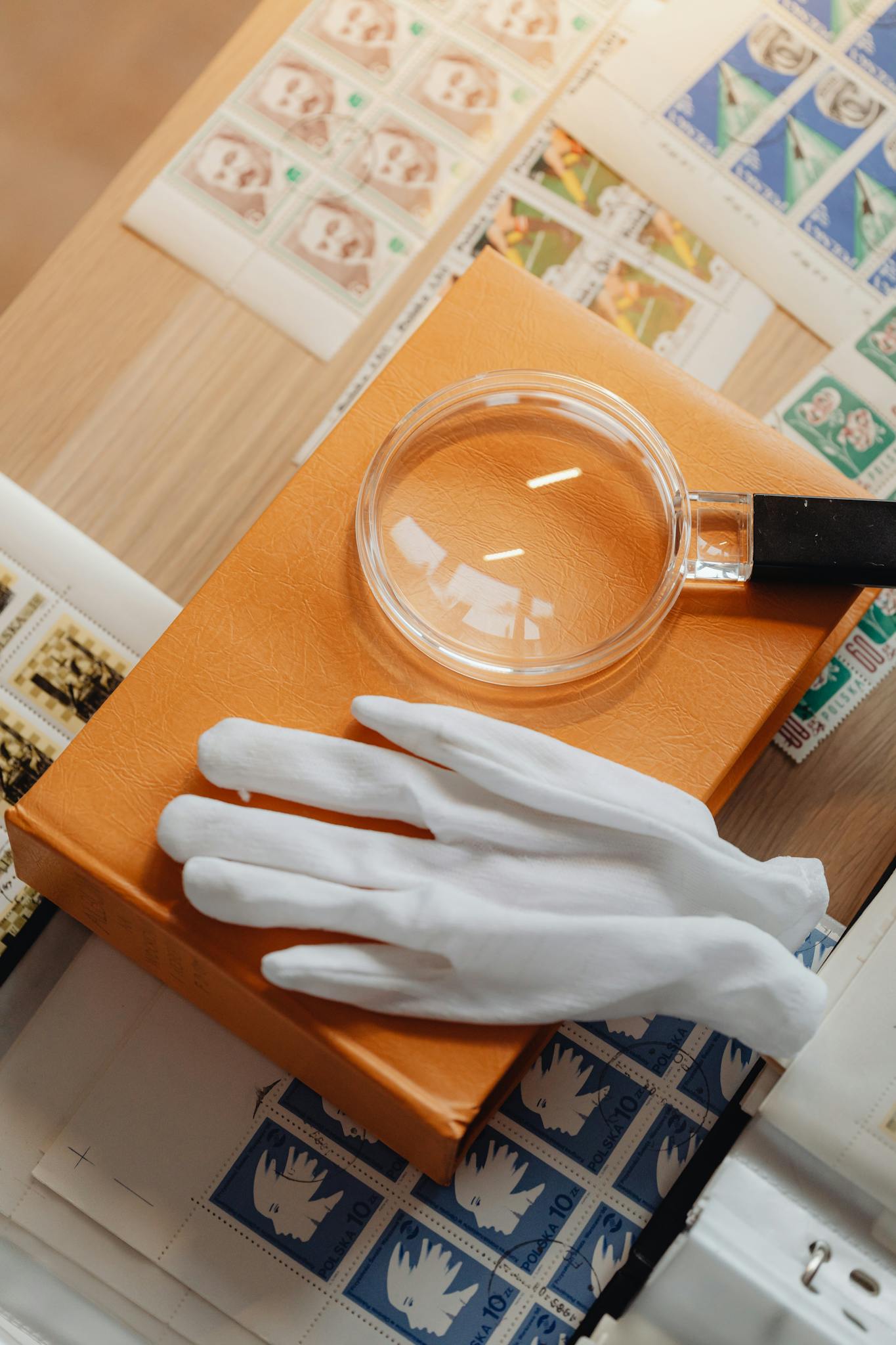 High angle view of a vintage stamp collection featuring a magnifying glass and gloves on a wooden surface.