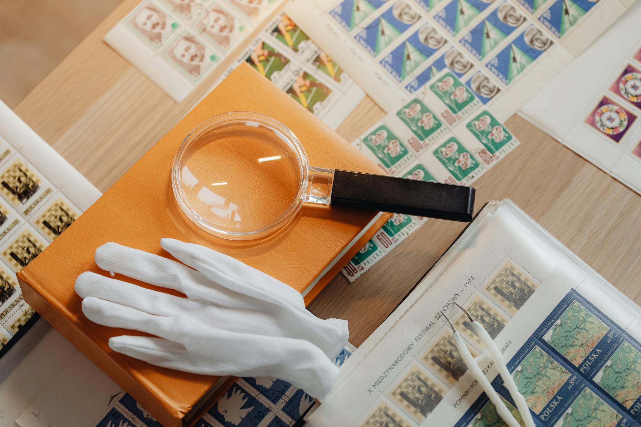 Magnifying glass, gloves, and stamp albums arranged on a wooden surface for collecting enthusiasts.