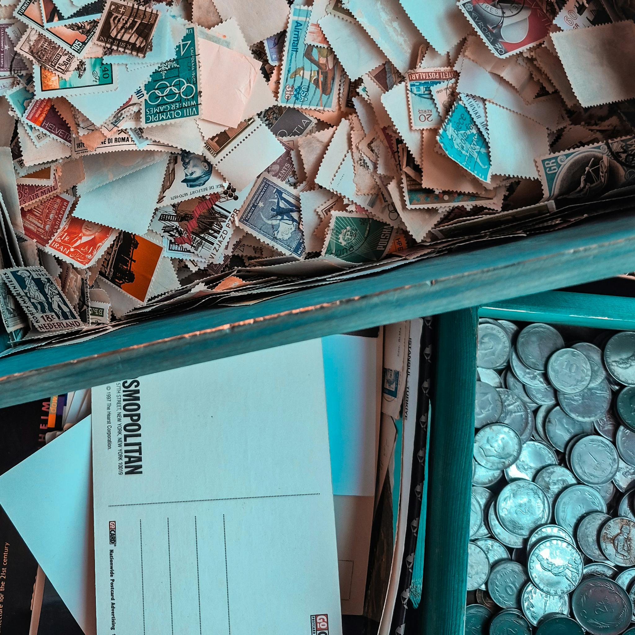 Top view of vintage stamps, postcards, and coins in a collector's box, showcasing nostalgia.
